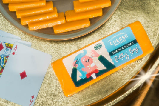 Slice of "Pretty Boy" Sharp Cheddar cheese by Cheese Brothers, Inc., showing its rich orange color and smooth texture.