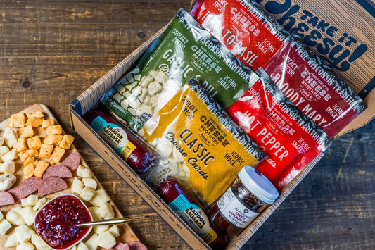 Cheese Brothers Inc. Char-CURD-erie Box gift set with assorted cheeses and curated cheese products on a wooden board.