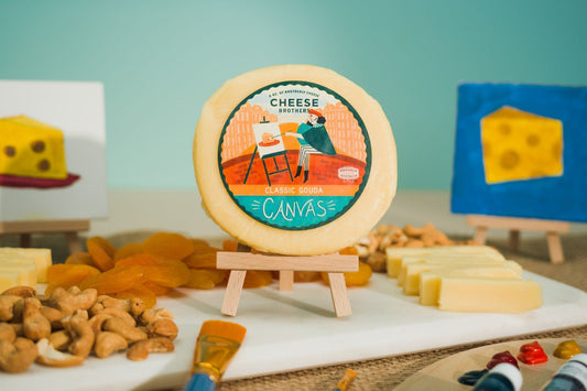 Creamy Classic Gouda cheese from Cheese Brothers, Inc. displayed on a wooden board with a wedge cut showing smooth, yellow cheese.
