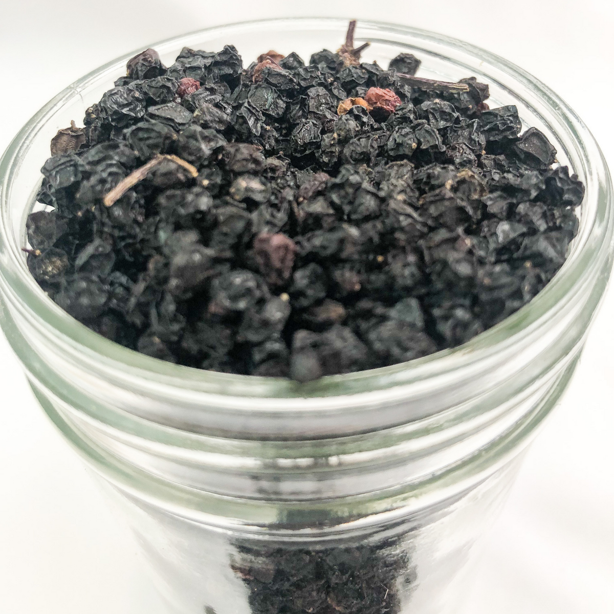 Close-up of herbalroseapothecary dried elderberry herb jar with a white background and clear label, showcasing small herbal jars.