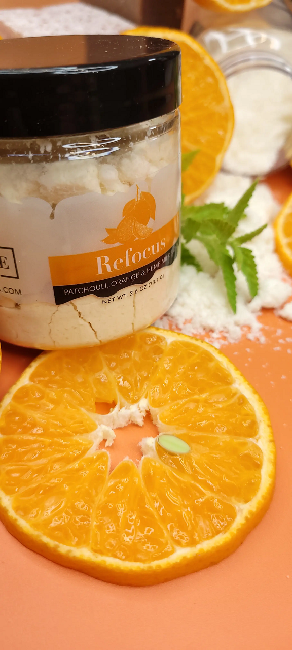 Mini Evolve Botanica Milk Bath Refocus with patchouli, orange, and hempseed oil, showing the relaxing bath product in a natural setting.