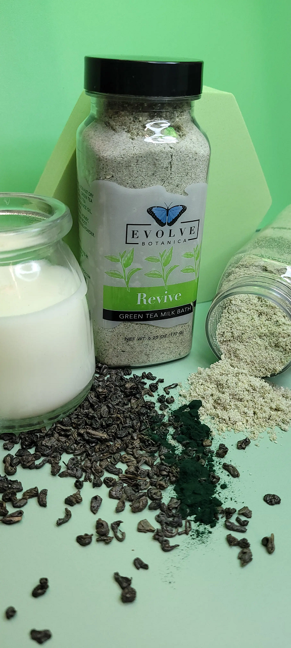 Evolve Botanica Revive Milk Bath with Green Tea in a glass jar, showing the product label and green tea leaves.
