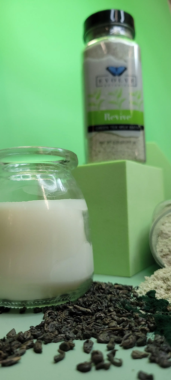 Evolve Botanica Milk Bath Revive with Green Tea, soothing powder in a clear jar with green tea leaves and milk bath ingredients.