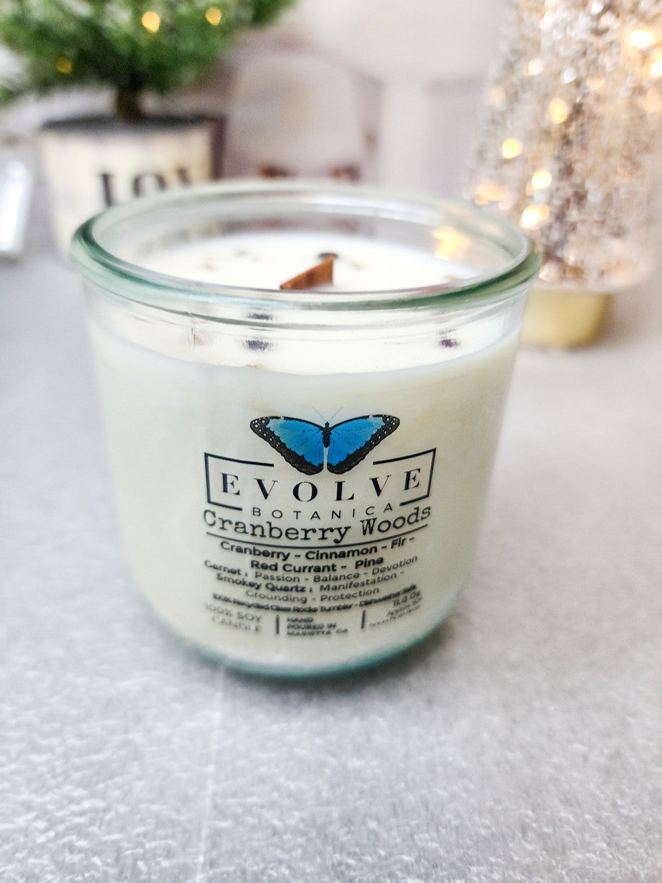 Evolve Botanica Cranberry Woods soy candle with wood wick, garnet, and smoky quartz gemstones, in a glass jar.