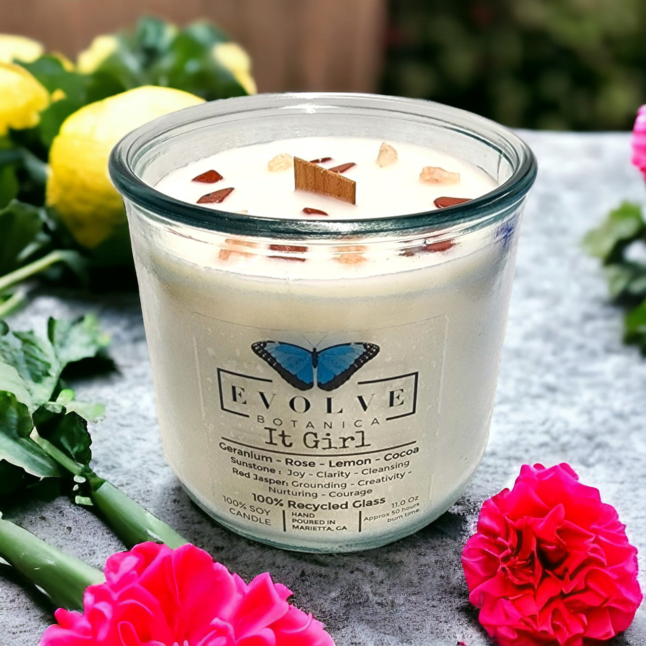 Evolve Botanica Rocks Candle It Girl with sunstone and red jasper gemstones, soy candle with wood wick, showcasing gemstones and candle flame.