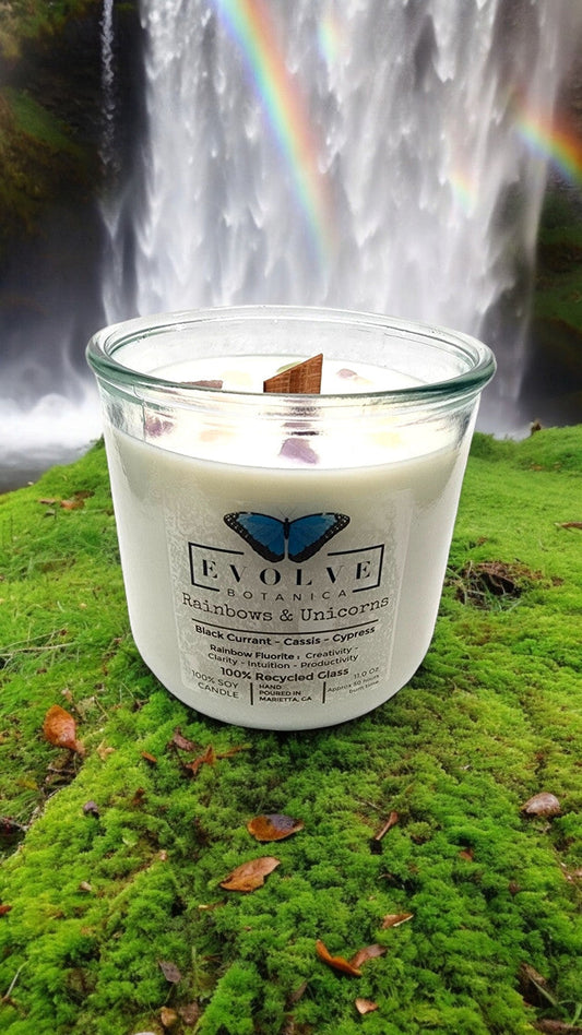 Evolve Botanica Rainbows & Unicorns soy candle with rainbow fluorite gemstone and wood wick, featuring colorful unicorn and rainbow design.
