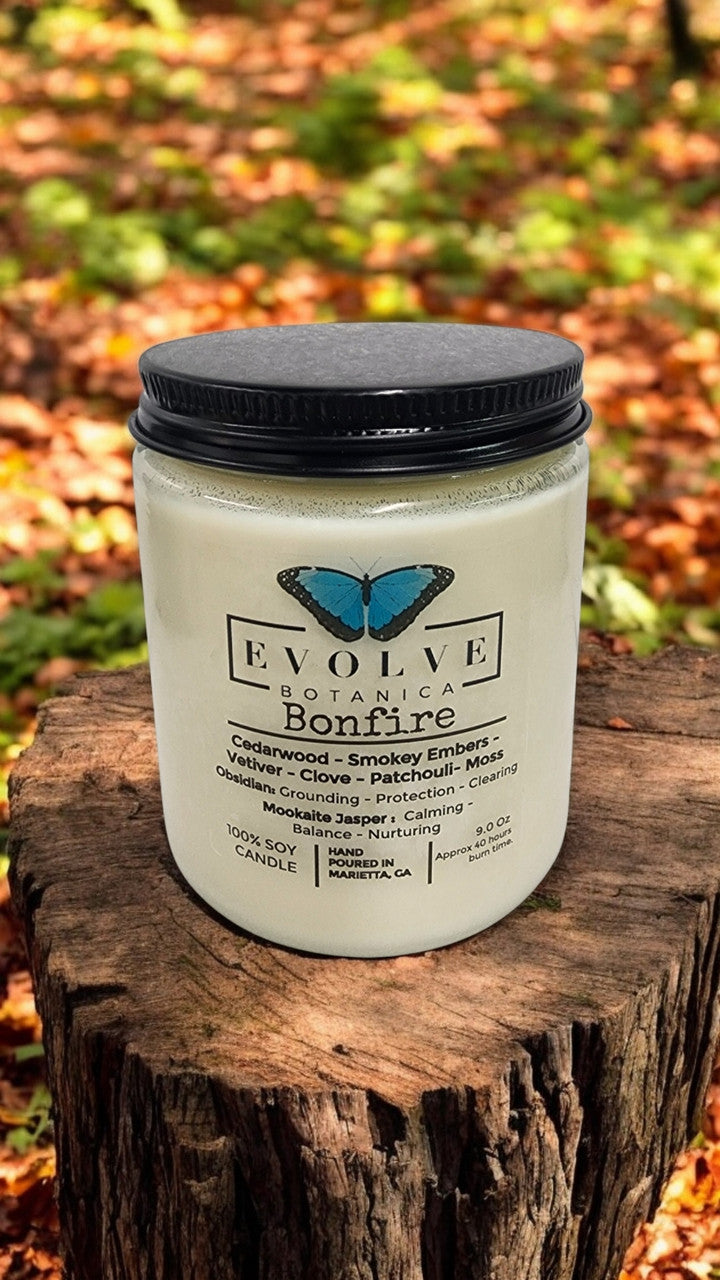 Classic 9oz jam jar soy candle by Evolve Botanica with obsidian and mookaite crystals, natural wood wick, and bonfire scent.