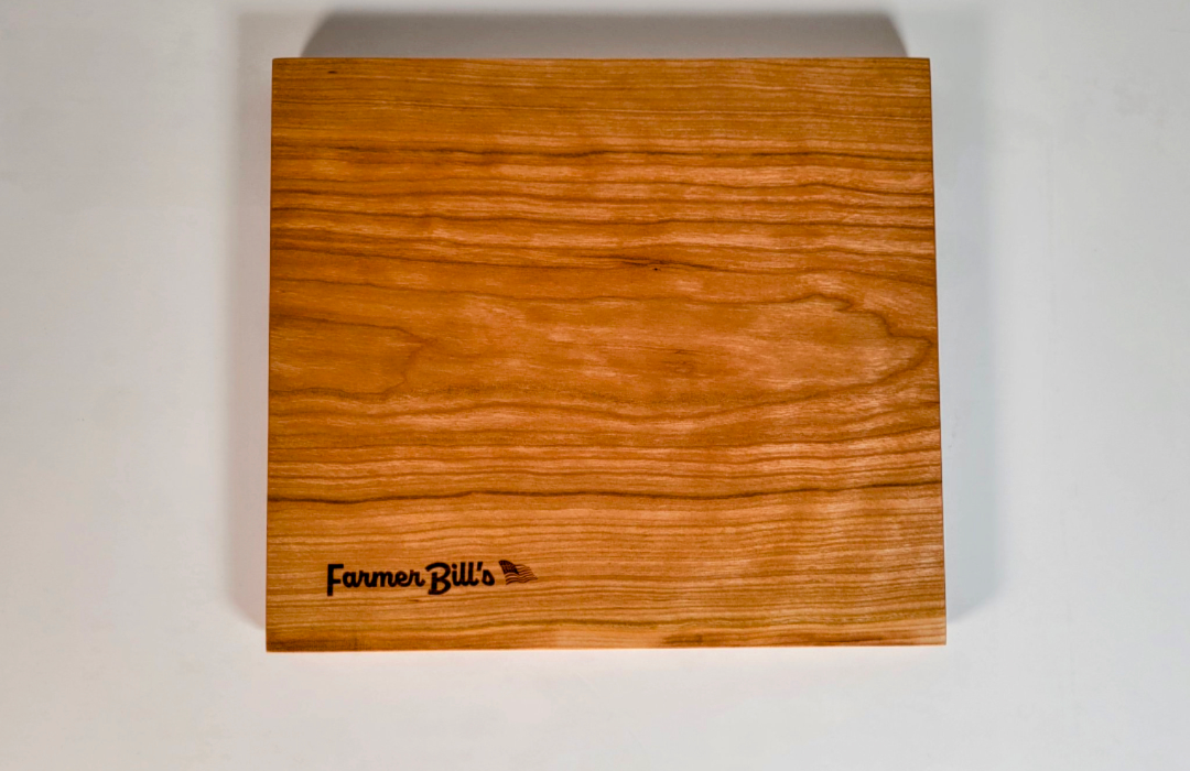 Cherrywood cutting board by Farmer Bill's Provisions, made and sourced in the USA, showing a smooth, polished wooden surface.