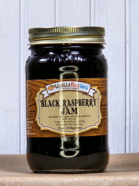 Black raspberry jam by Georgia Peach World in a glass jar with fresh raspberries, showcasing its rich, dark color and fruit texture.