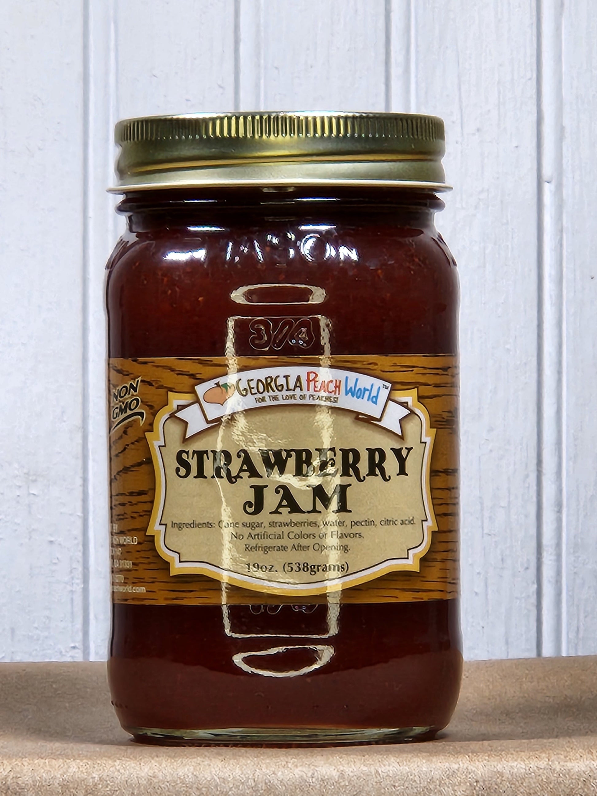 Glass jar of Georgia Peach World strawberry jam with a spoonful showing the bright red, chunky fruit spread.
