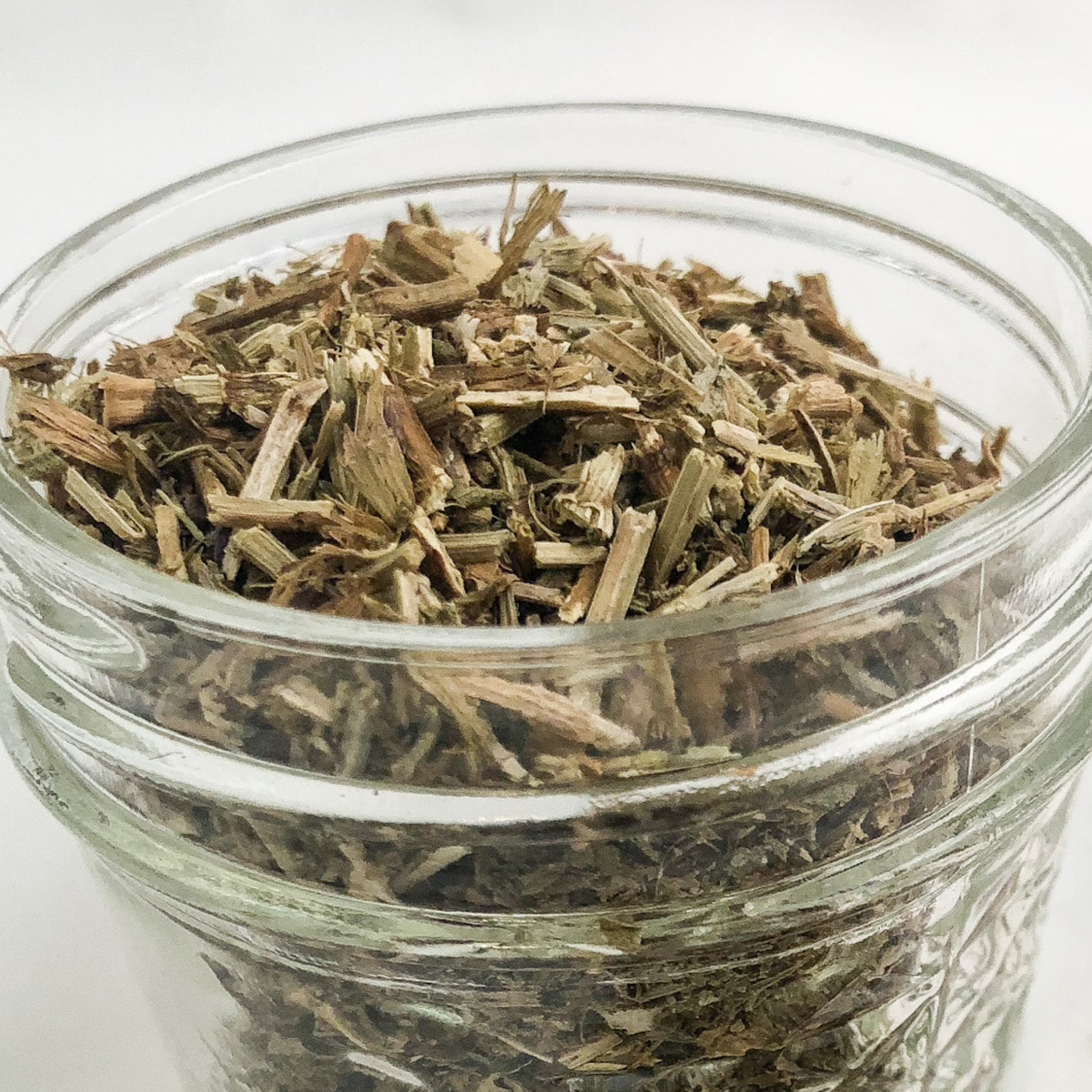 Close-up of a white jar of dried hyssop herbs in a small herbalroseapothecary jar, showcasing fresh herb details.