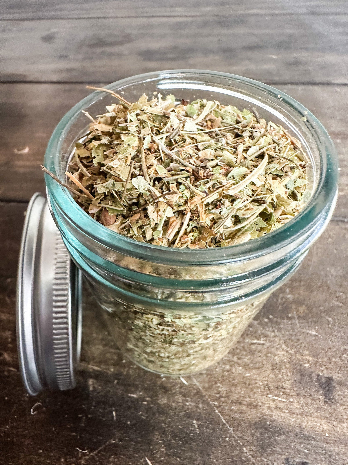 Small glass jar of dried herbs from HerbalRoseApothecary, featuring a label and a small herbal jar for herbal remedies.