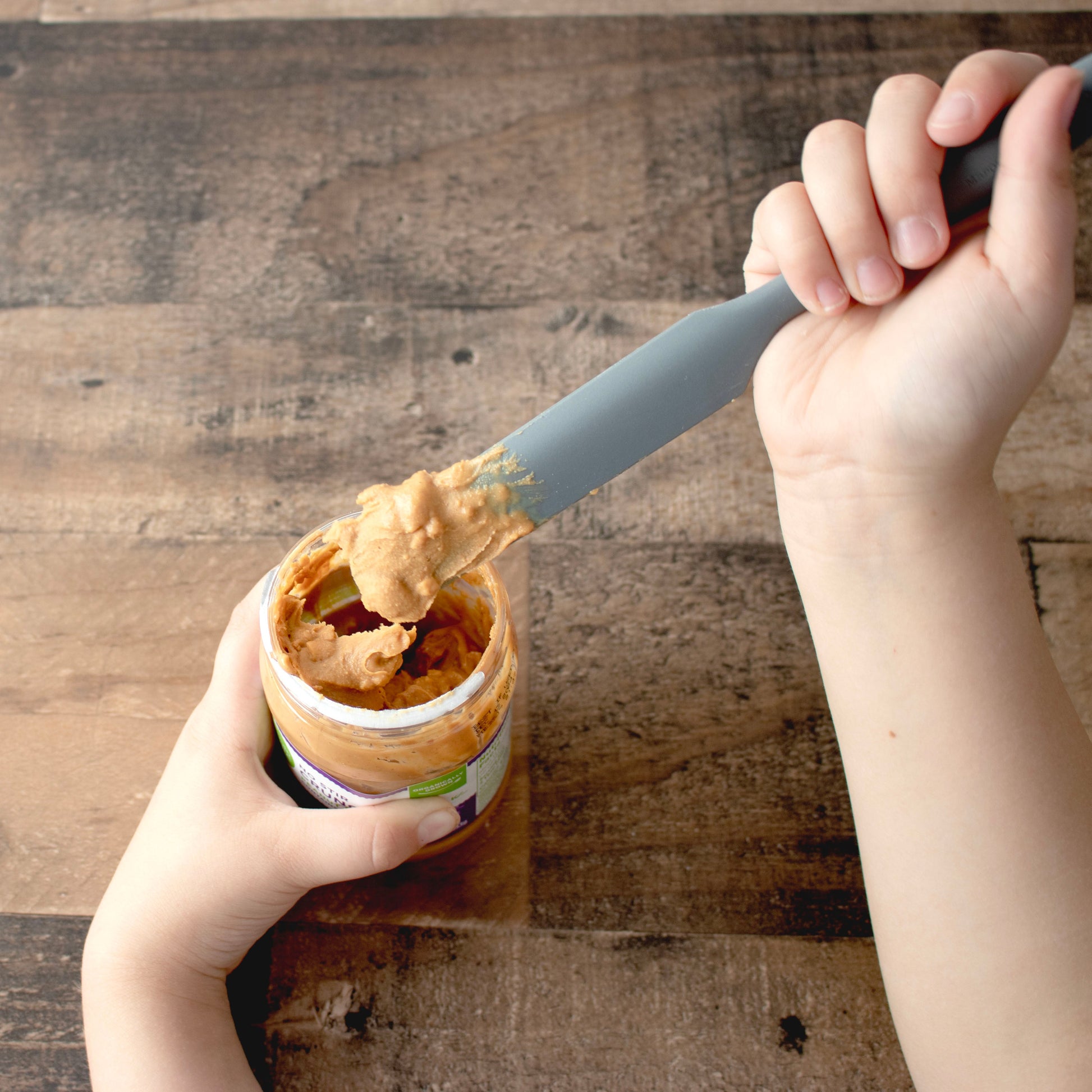 Charcoal gray silicone jar scraper from Mason Jar Lifestyle used to scoop peanut butter from a jar.