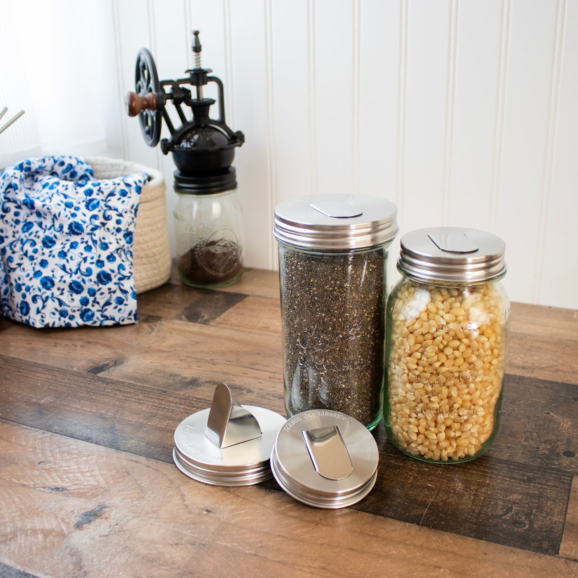 Two stainless steel grain dispenser lids for regular-mouth mason jars, compatible with Mason Jar Lifestyle jars.