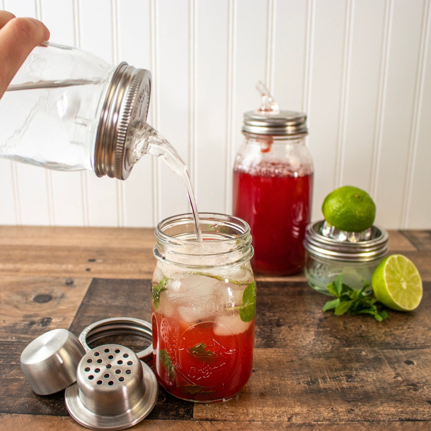 Mason Jar Lifestyle stainless steel cocktail shaker lid with band, shown with lime, strawberry syrup, and ice for mixed drinks.