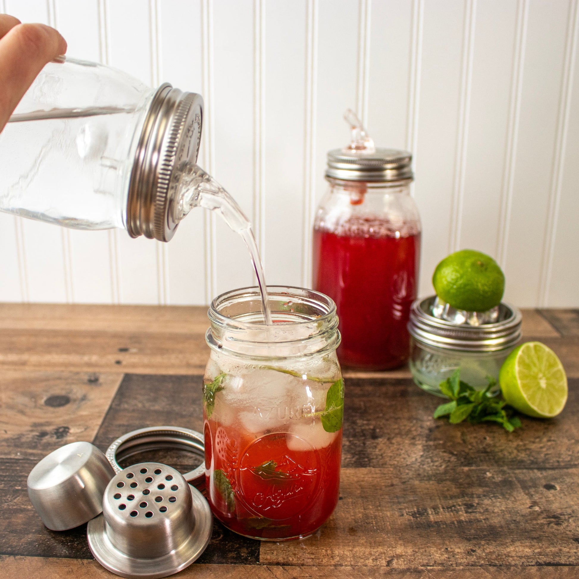 Mason Jar Lifestyle stainless steel cocktail shaker lid with band, shown with lime, strawberry syrup, and ice for mixed drinks.