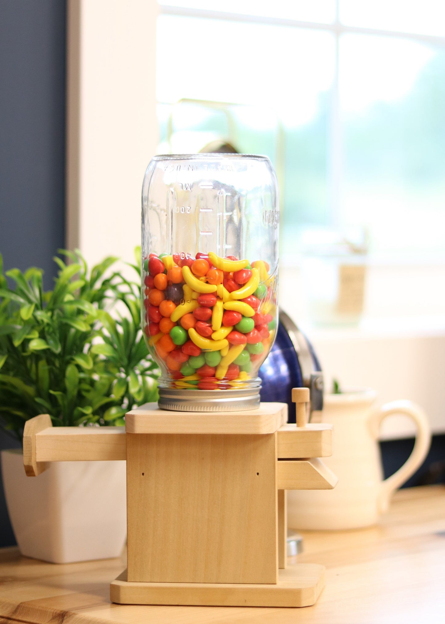 Colorful AmishToyBox.com candy dispenser toy with jar for M&Ms, peanuts, or jelly beans, featuring a playful design and bright colors.