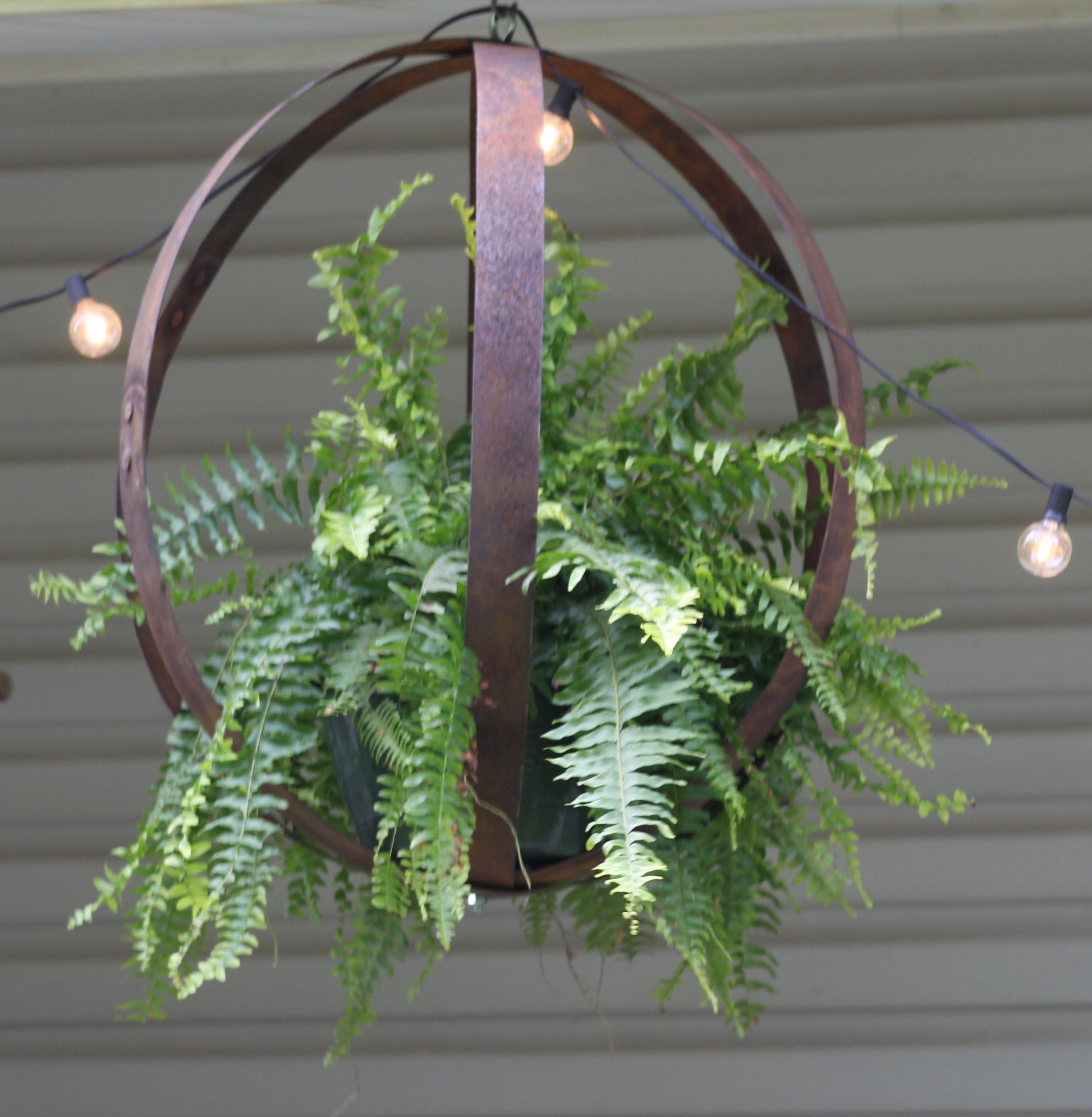Rustic hanging plant holder made from reclaimed whiskey barrel rings, outdoor decor with a natural, handcrafted look.