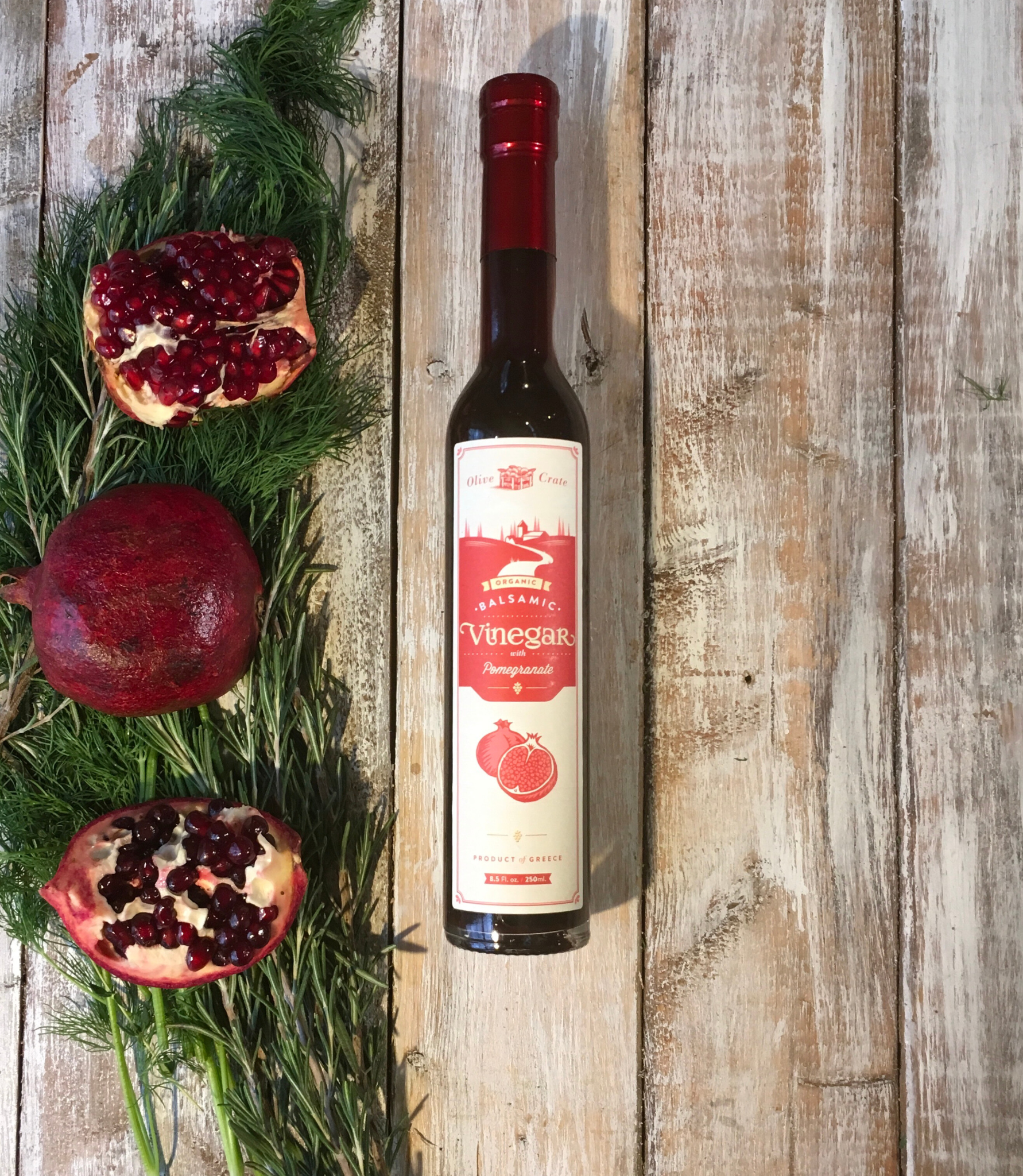 Glass bottle of Olive Crate 100% organic balsamic vinegar with pomegranate, featuring dark balsamic and pomegranate seeds inside.