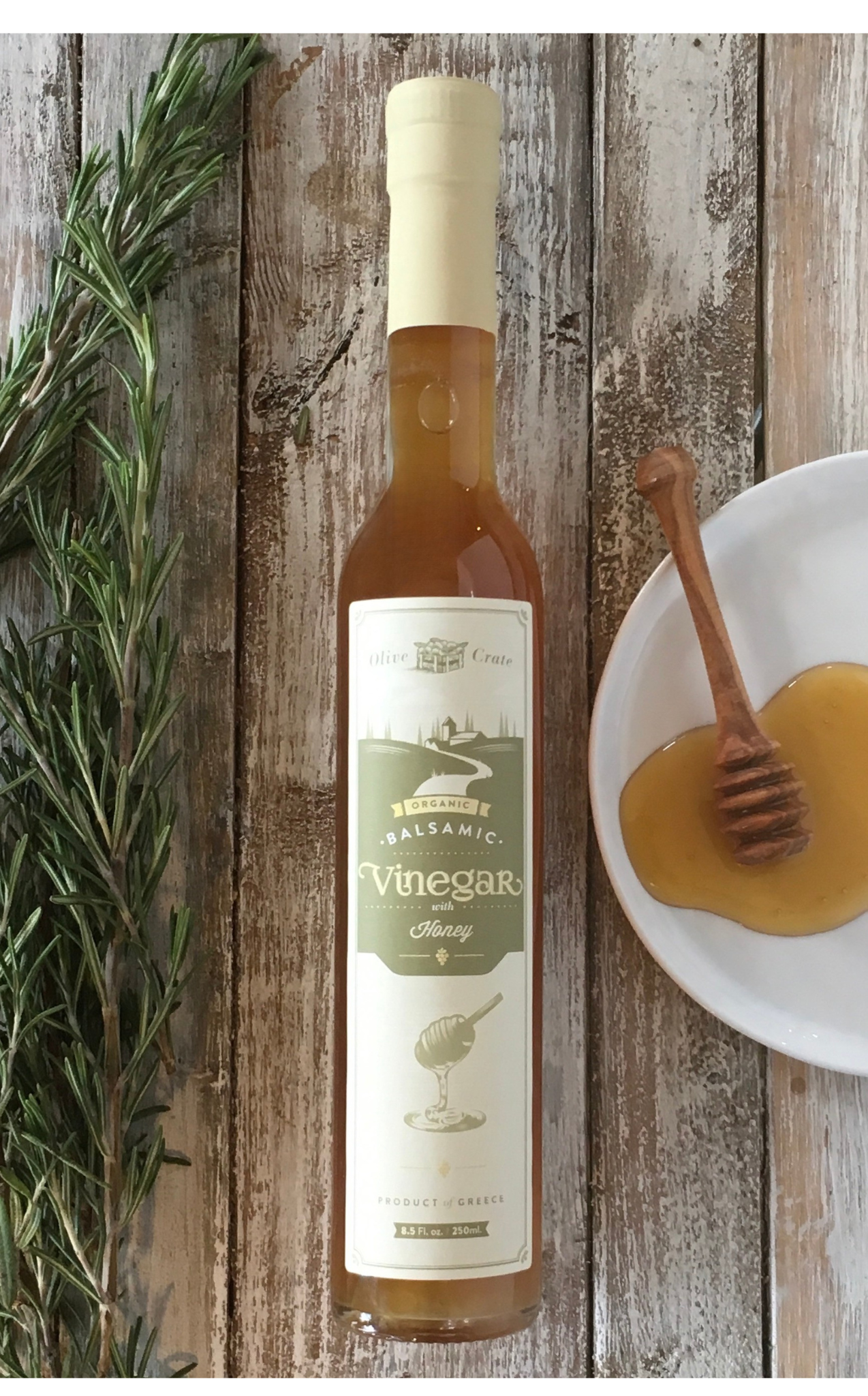 Glass bottle of Olive Crate 100% organic white balsamic vinegar with honey, showcasing the clear liquid and elegant packaging.