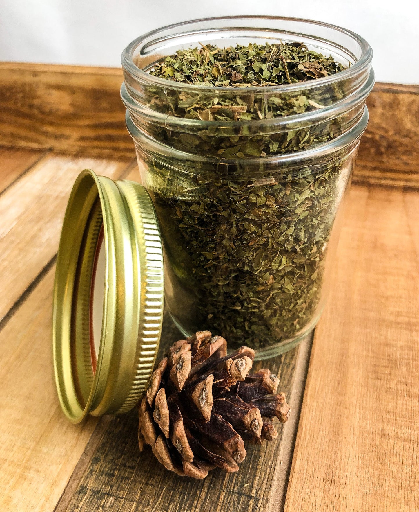 Small herbal jar containing dried peppermint herbs, with a wood and white label design from herbalroseapothecary.