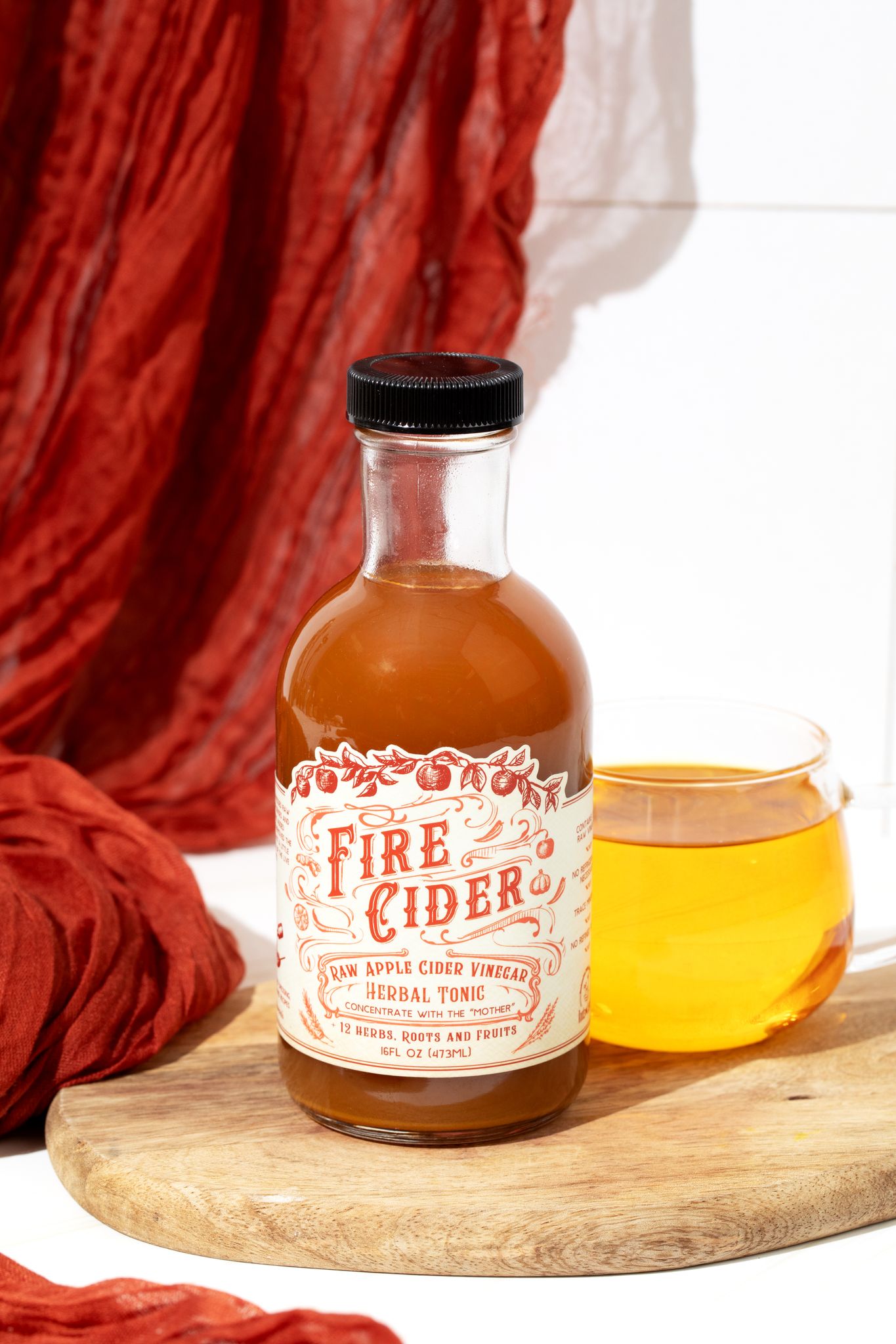 16 oz bottle of Fire Cider by Roots and Leaves LLC, featuring a dark glass bottle with a label and fresh ingredients visible.