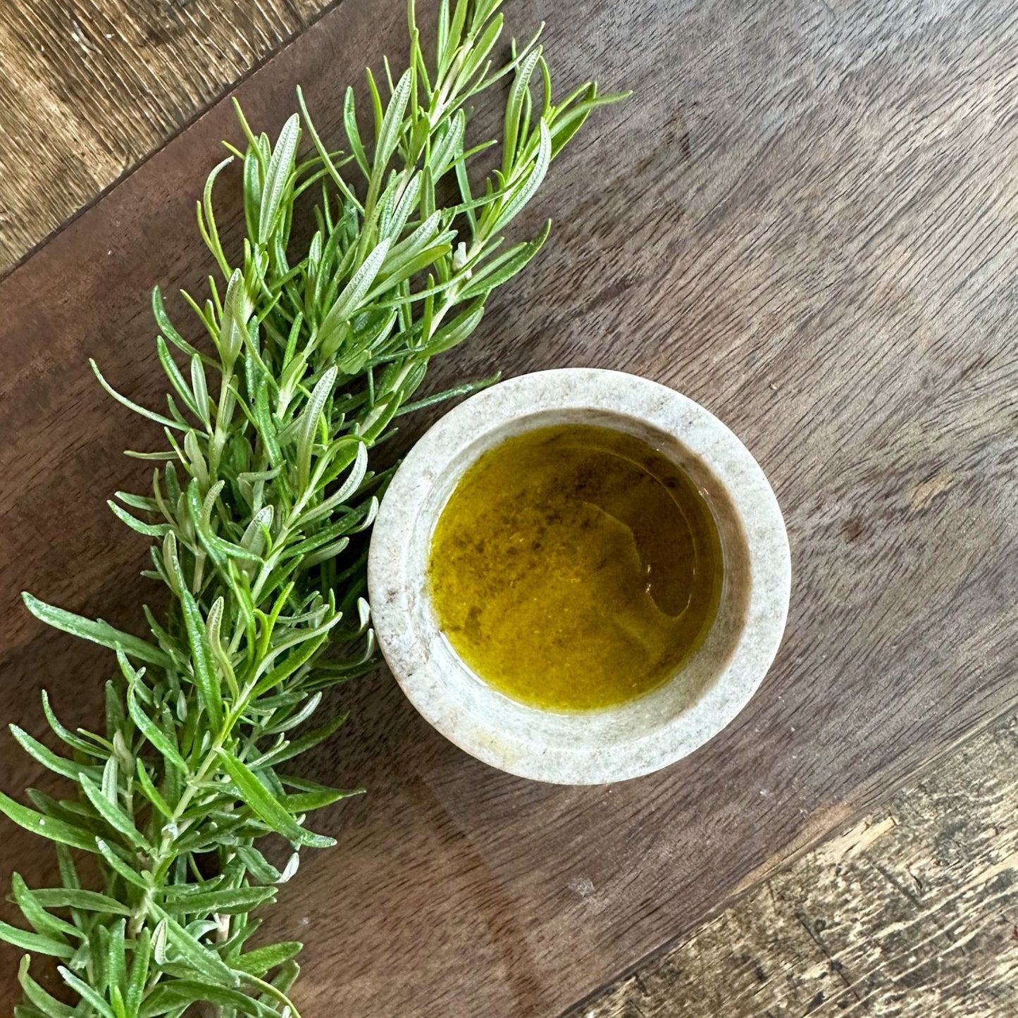 Bottle of Olive Branch Oil & Spice Rosemary Fused Extra Virgin Olive Oil with fresh rosemary sprigs and olive oil in clear glass bottle
