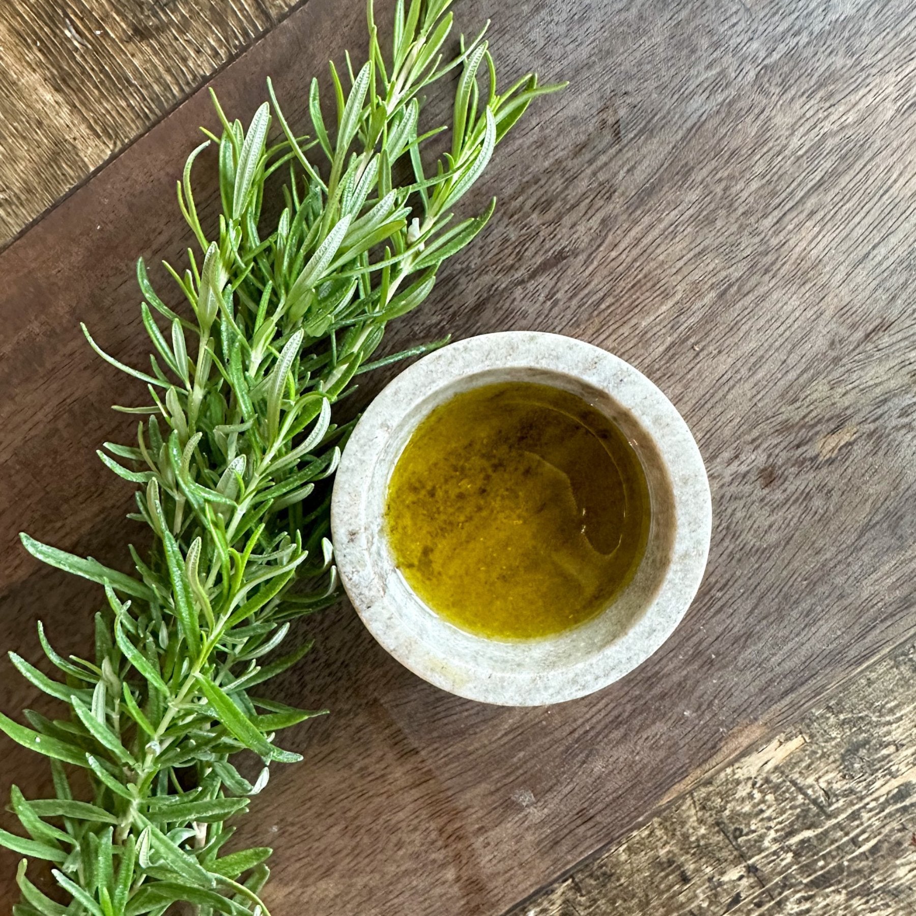 Bottle of Olive Branch Oil & Spice Rosemary Fused Extra Virgin Olive Oil with fresh rosemary sprigs and olive oil in clear glass bottle