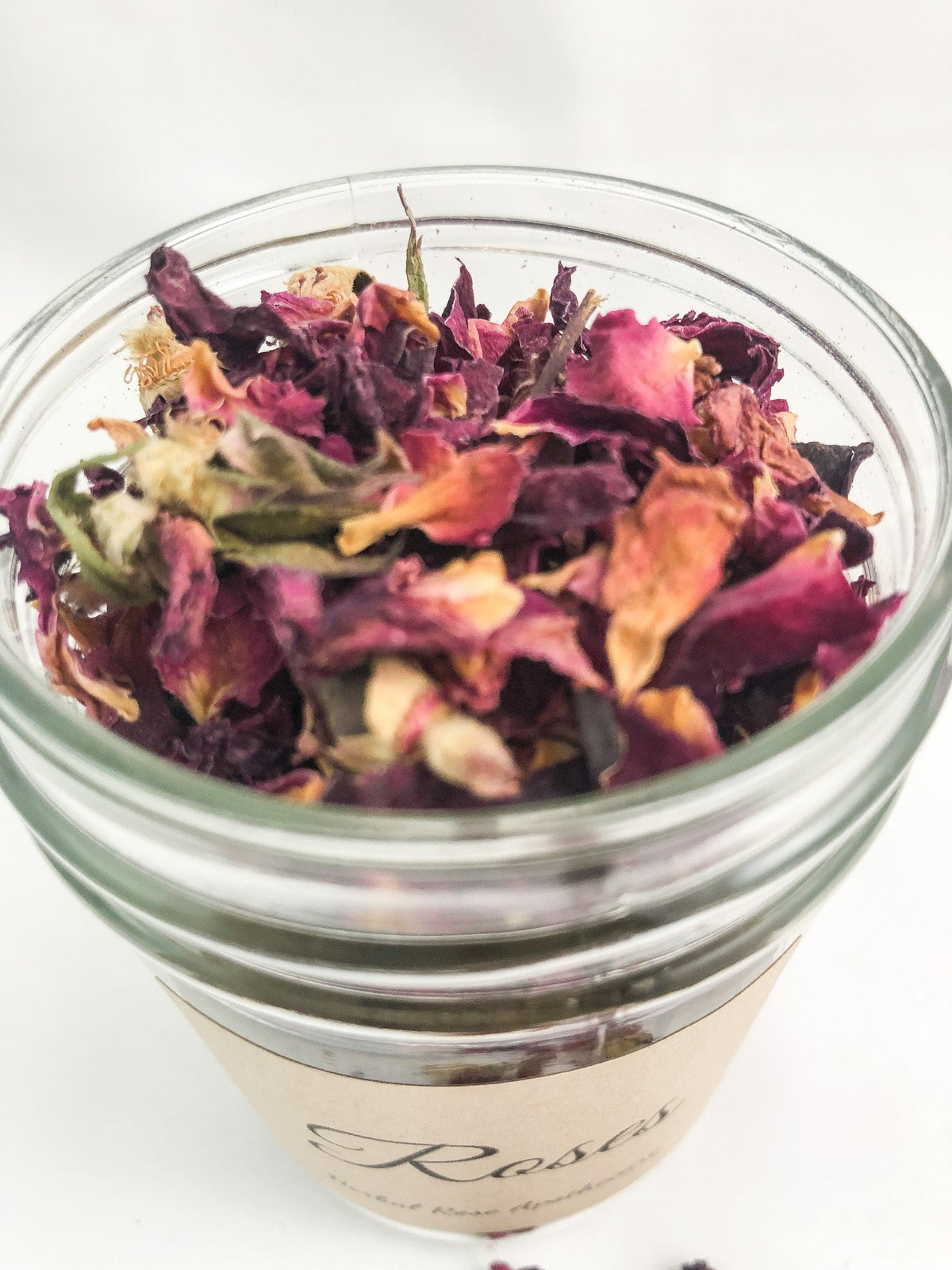 Small white jar of dried herbs from HerbalRoseApothecary, featuring a clear label and a rustic wooden background.