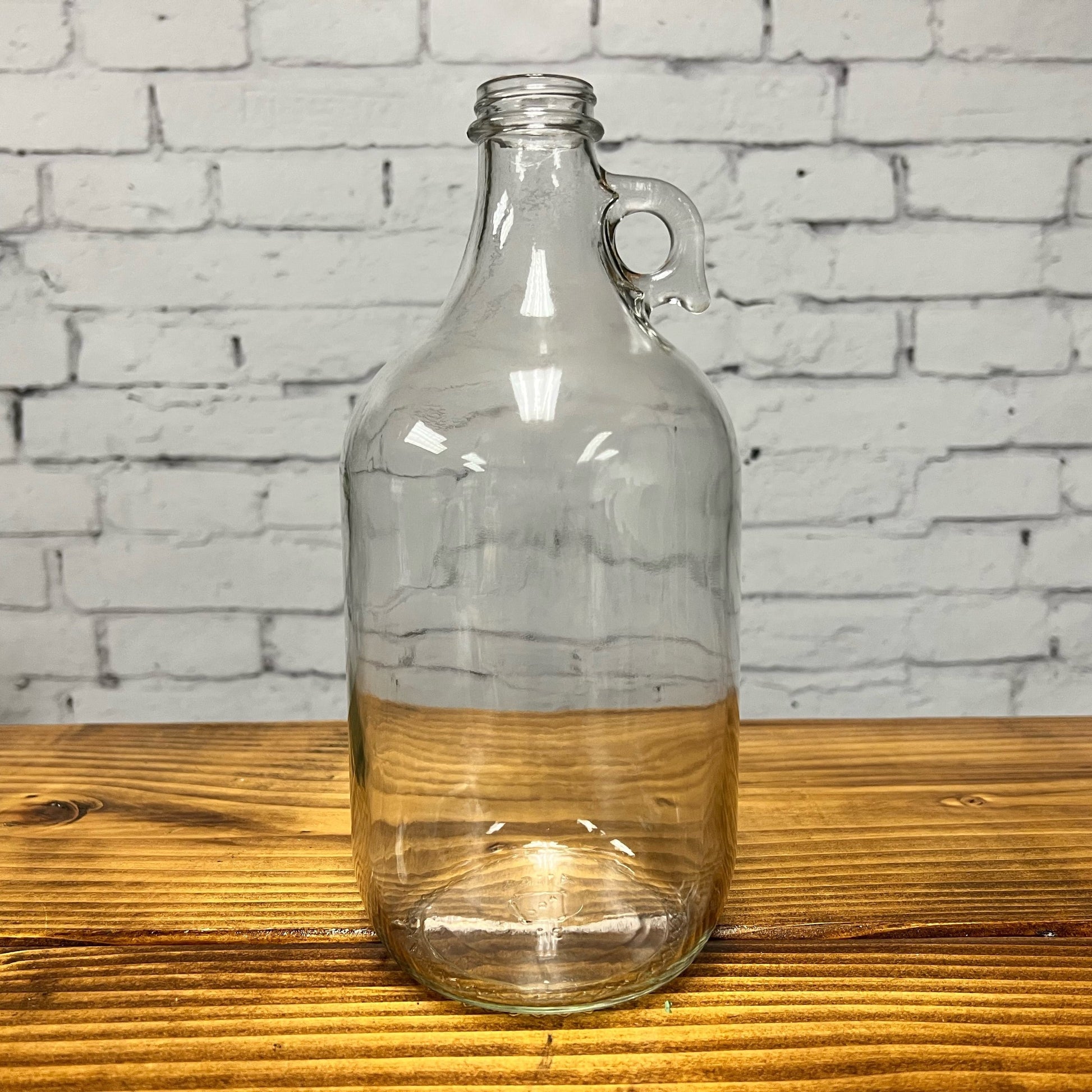 Half-gallon glass jug with cap from Rustic Strength, a durable container for liquids with a clear glass body and secure lid.