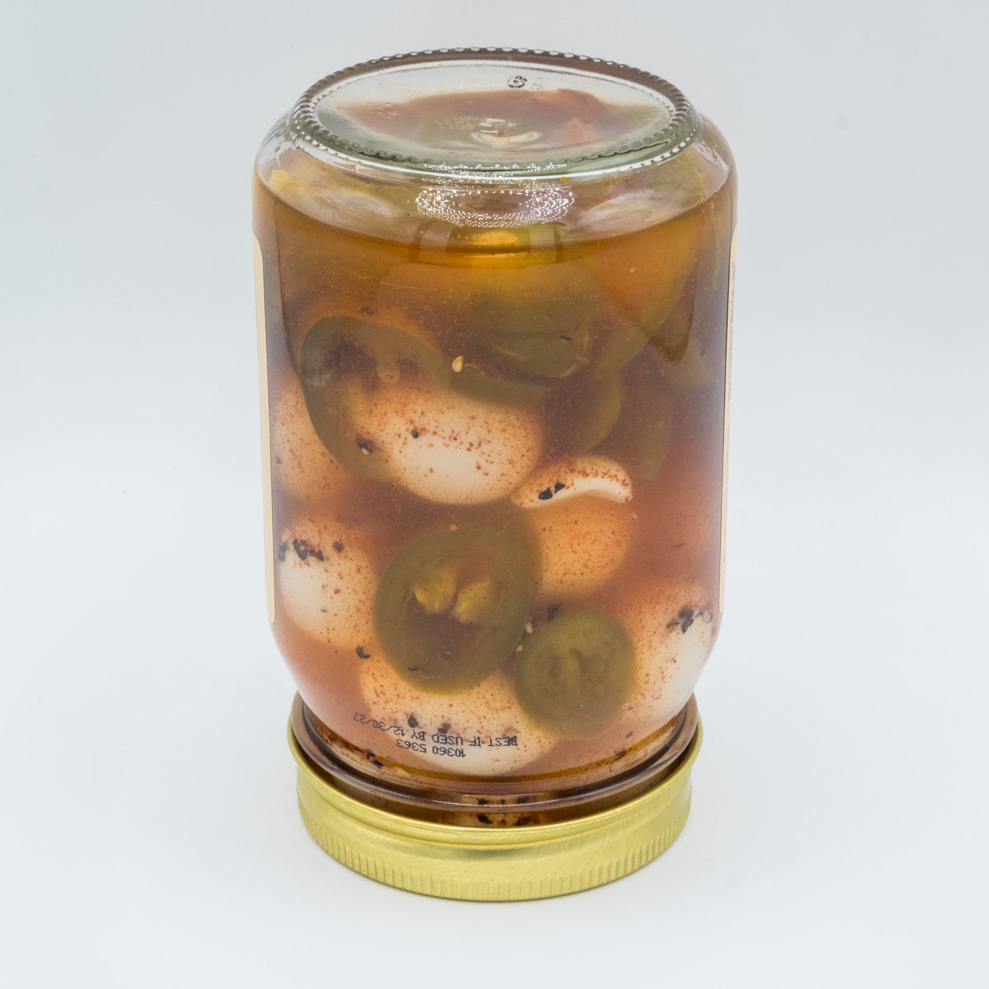 Canned spicy pickled quail eggs from Amish Country Store, showing a close-up of the jar with vibrant peppers and eggs inside.