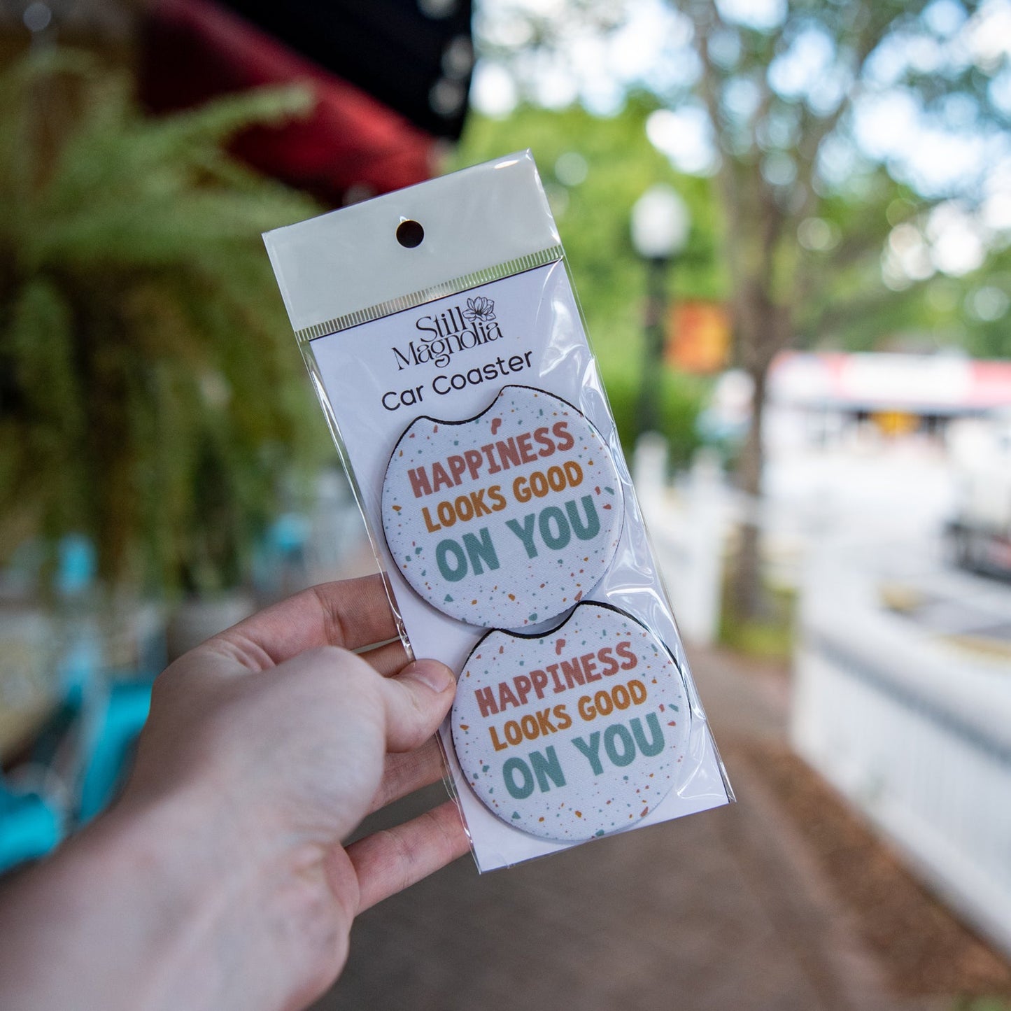 Still Magnolia car coaster featuring the "Happiness Looks Good on You" design, durable cork material, perfect for car cup holders.