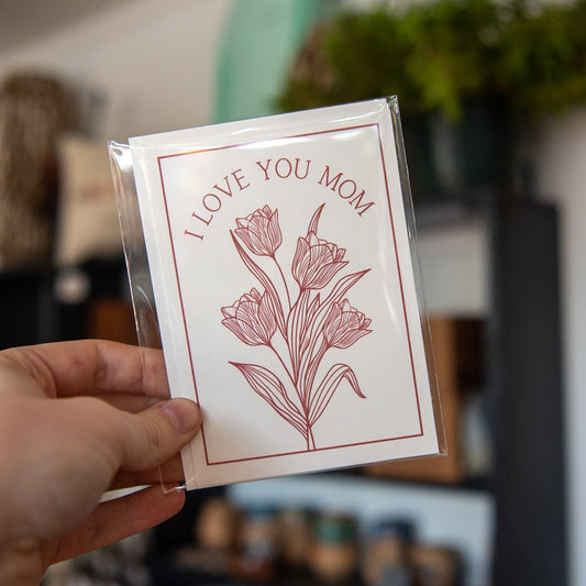 Still Magnolia "I Love You Mom" card with floral design, featuring heartfelt message, perfect for Mother's Day or special occasions.