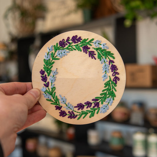 Lavender wreath embroidery kit by Still Magnolia featuring fabric, embroidery hoop, and lavender-colored thread for detailed stitching.
