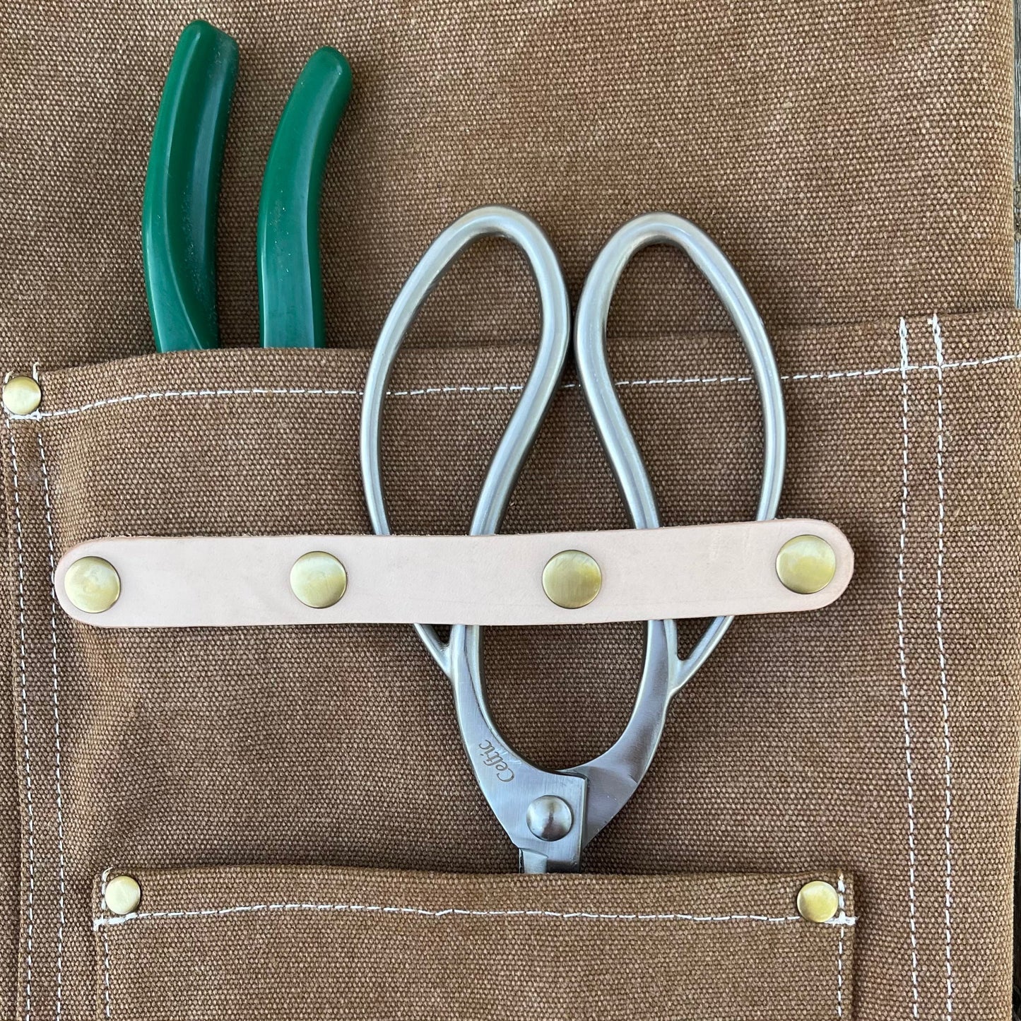 Dark green waxed canvas gardening apron with multiple pockets from The Celtic Farm, designed for outdoor gardening tasks.