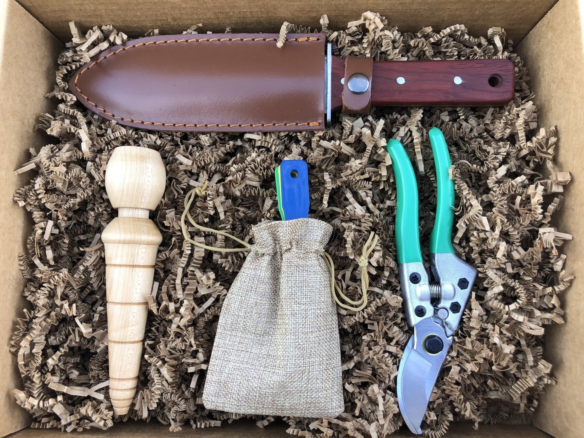 The Celtic Farm Ultimate Garden Gift Box with four garden tools including a hori hori, pruners, dibbler, and tool sharpeners.