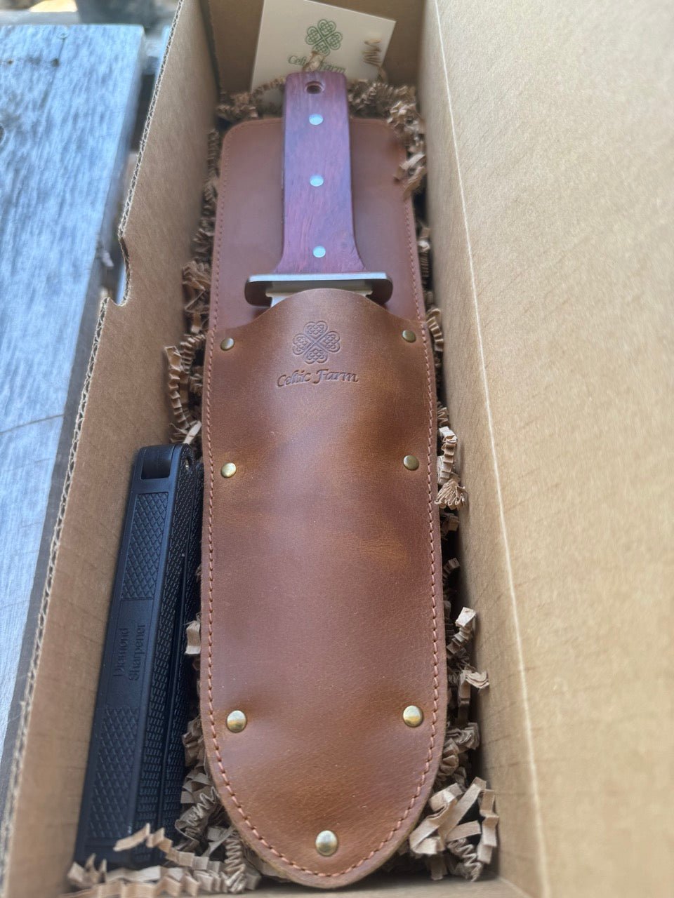 The Celtic Farm Hori Hori garden tool in a gift box, with a sharp blade and wooden handle, ideal for gardening and planting tasks.