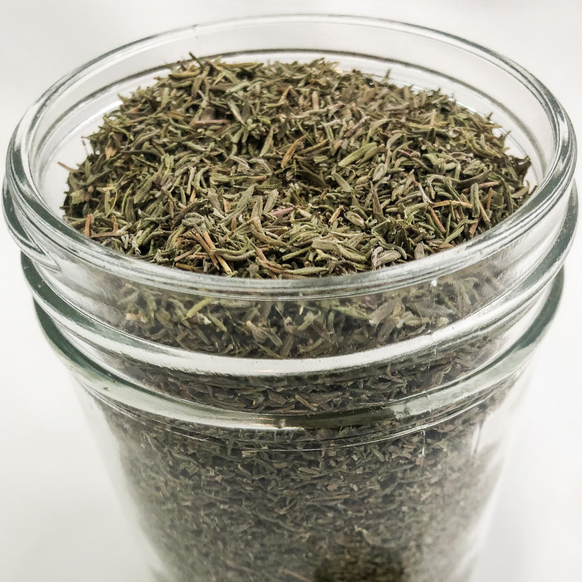 Small jar of dried thyme herbs from herbalroseapothecary, close-up view showcasing the jar and thyme inside.