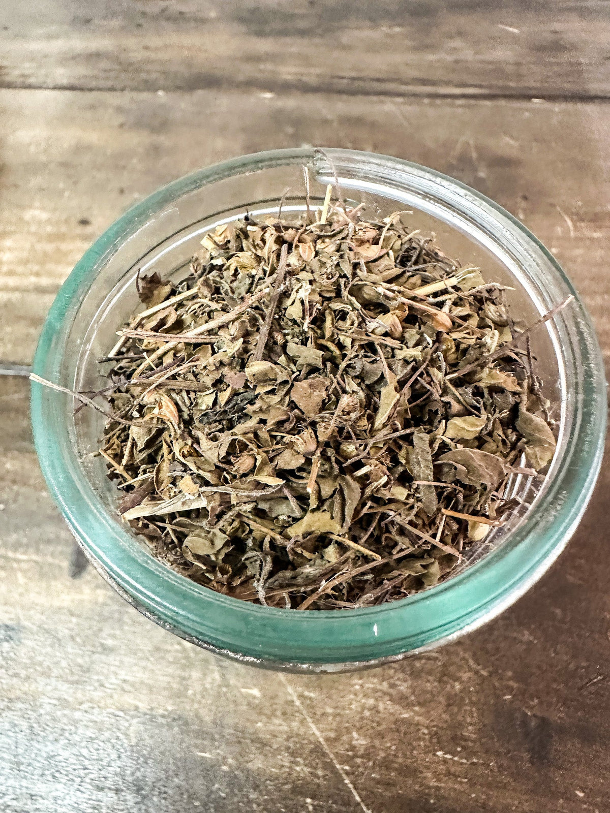 Small herbal jars with dried tulsi herbs from HerbalRoseApothecary, showcasing mini glass jars filled with fresh green tulsi leaves.