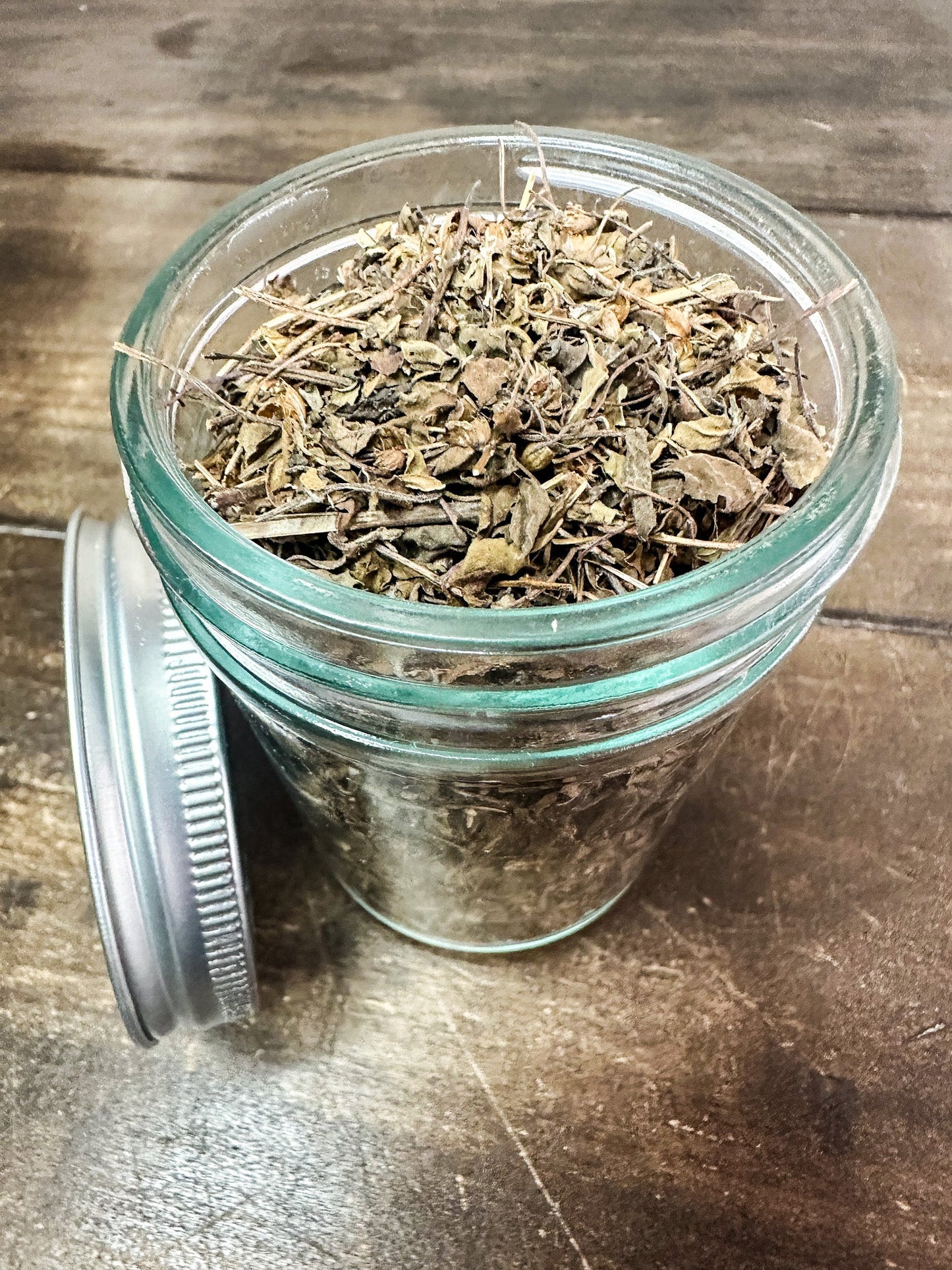 Small jar of dried tulsi herbs from HerbalRoseApothecary, showcasing the herb's vibrant green leaves in a clear jar.
