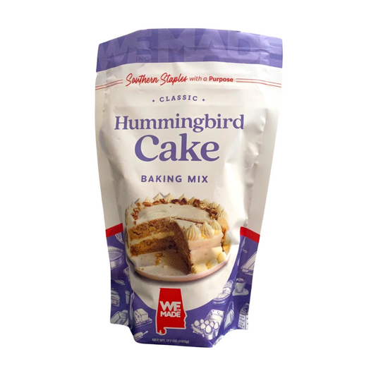Box of WE Made Hummingbird Cake Mix with fresh ingredients and colorful packaging, ready for baking.