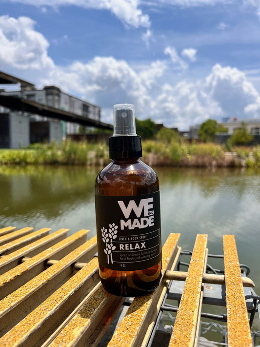 WE Made Relax Linen & Room Spray bottle with a white label and spray nozzle, designed to refresh linens and room spaces.